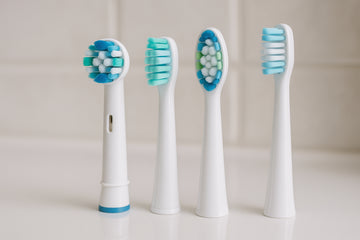 Close-up of different electric toothbrush replacement heads arranged on a clean bathroom counter. Alt: Electric toothbrush replacement heads variety for optimal oral care.